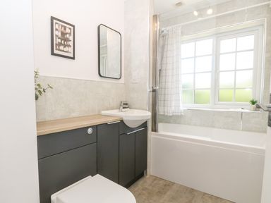 A bathroom with a bathtub a shower curtain a sink a mirror and a framed picture at Glan Dwr in Red Wharf Bay