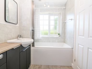 A bathroom with a bathtub next to a window and a sink with cabinets beneath at Glan Dwr in Red Wharf Bay