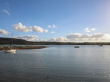 A body of water with boats and a small land area with hills and scattered buildings in the background at Glan Dwr in Red Wharf Bay