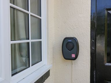 An electric vehicle charging station mounted on an exterior wall between a window and a black door at Glan Dwr in Red Wharf Bay