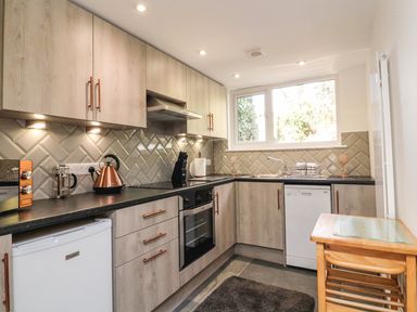 A kitchen with wooden cabinets a black countertop a white dishwasher a refrigerator an oven a kettle knives and a window at Easterly Cottage in Bude