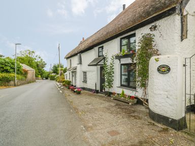 An exterior view of a thatched cottage with white walls and flower pots along the sidewalk at Easterly Cottage in Bude