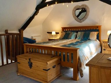 A bedroom with a wooden bed and chest under sloped ceiling with exposed beams at Easterly Cottage in Bude