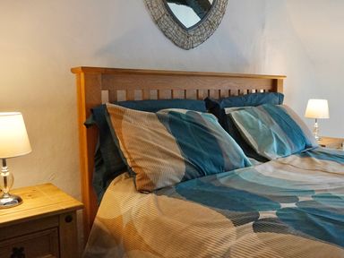A bedroom with a wooden bed frame striped bedding bedside tables and lamps at Easterly Cottage in Bude