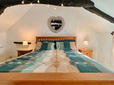 A bedroom with a double bed two bedside tables with lamps and a heart shaped mirror on the wall at Easterly Cottage in Bude