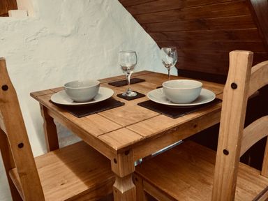 A wooden dining table set for two with bowls plates and wine glasses at Easterly Cottage in Bude