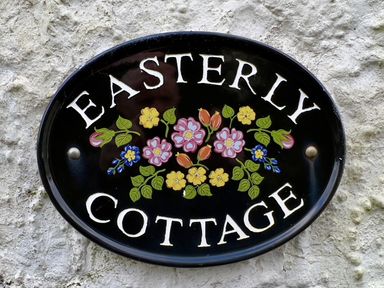 A black oval sign with the words Easterly Cottage and floral decorations on a textured wall at Easterly Cottage in Bude