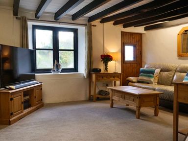 A living room with a sofa a wooden coffee table a television on a wooden stand and a side table with flowers at Easterly Cottage in Bude