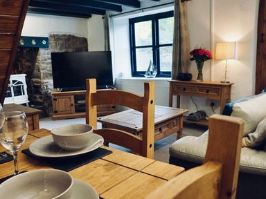 A living room with wooden furniture bowls on a table and a television at Easterly Cottage in Bude