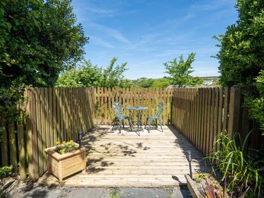 A garden with a wooden deck surrounded by a fence at Easterly Cottage in Bude
