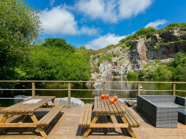 An outdoor area with a picnic table and seating near a lake at Costentyn, Tor Down Quarry in St Breward