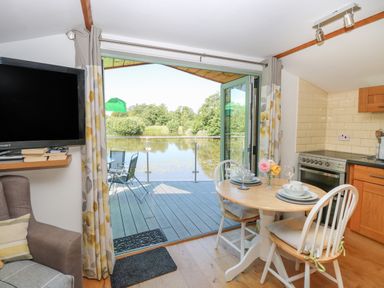 A kitchen dining area with a round table set for two and an open door leading to a deck overlooking a lake at Lakeside Lodge East Harling near Thetford