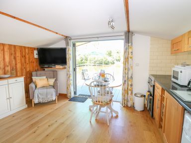 A small kitchen and dining area with a table and chairs and an armchair next to a wall-mounted television at Lakeside Lodge East Harling near Thetford