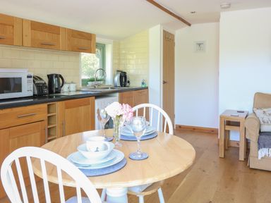 A kitchen and dining area with wooden cabinets a round dining table set with dishes and glasses at Lakeside Lodge in East Harling near Thetford