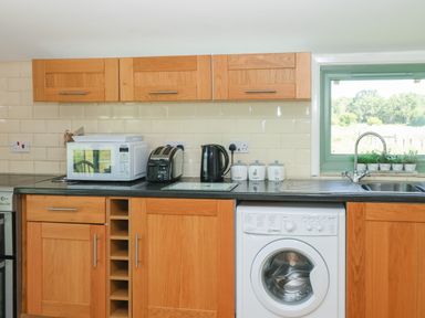 A kitchen with wooden cabinets a microwave toaster kettle washing machine and a window with plants at Lakeside Lodge in East Harling near Thetford