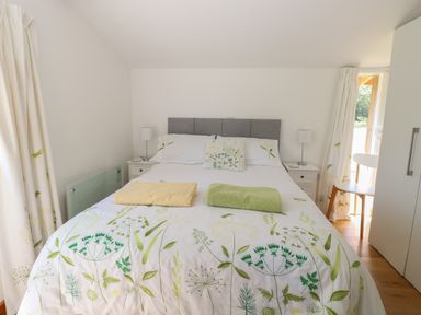 A bedroom with a bed with floral bedding two bedside tables with lamps curtains and a chair at Lakeside Lodge in East Harling near Thetford