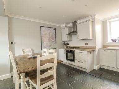 A kitchen with a wooden dining table white chairs white cabinets a stove and a map on the wall at Ivy Bank in Windermere