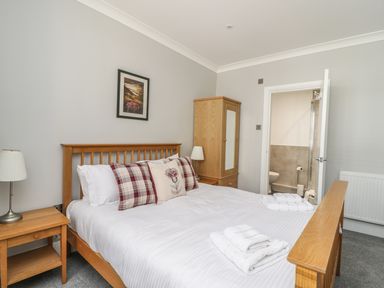 A bedroom with a wooden bed, bedside tables with lamps, a wardrobe, and an en suite bathroom at Ivy Bank in Windermere