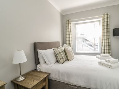 A bedroom with a bed with pillows and towels next to a window with curtains and a nightstand with a lamp at Ivy Bank in Windermere