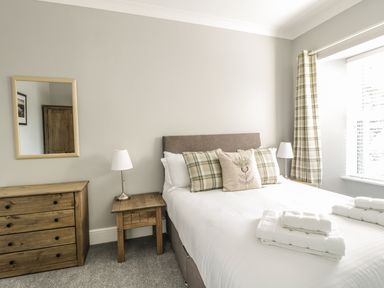 A bedroom with a bed with pillows bedside tables table lamps a dresser and a mirror at Ivy Bank in Windermere