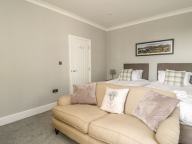 A bedroom with two single beds and a beige couch with pillows at Ivy Bank in Windermere