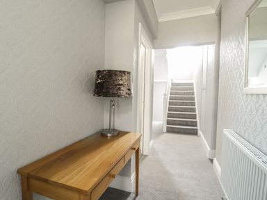 A hallway with a wooden table and lamp next to carpeted stairs at Ivy Bank in Windermere