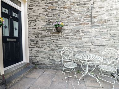 An outdoor area with a black door numbered 86 a hanging basket with flowers and a white metal table with two matching chairs at Ivy Bank in Windermere