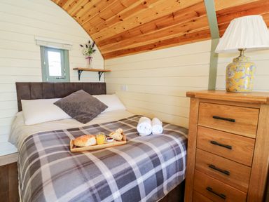 A bedroom with a bed covered by a checkered blanket and a wooden drawer with a lamp at Meadow View in Rhayader