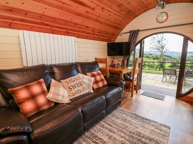 A living area with a leather sofa and cushions next to a dining table and chairs by glass doors opening to a patio in Meadow View Rhayader