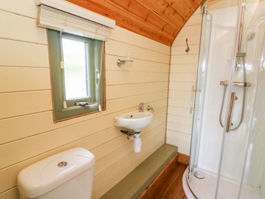 A small bathroom with a toilet, wall-mounted sink, window, and a curved glass shower enclosure at Meadow View in Rhayader