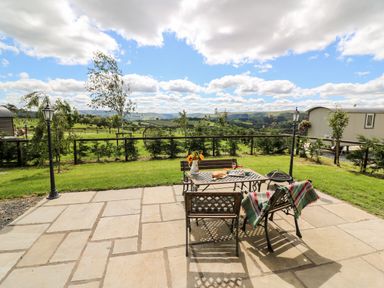 An outdoor patio with a metal table and chairs overlooking a green field at Meadow View in Rhayader
