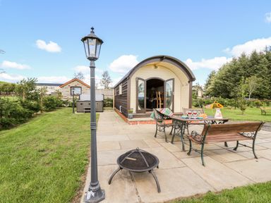 An outdoor patio with a table and benches with a small building and lamp posts in a garden at Meadow View in Rhayader