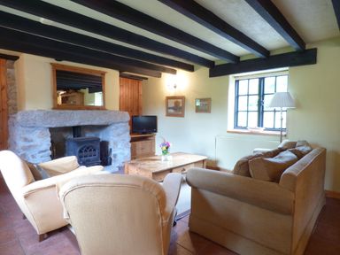 A living room with armchairs a sofa a wooden coffee table a stone fireplace and a window at Old Winery Cottage Golant near Fowey