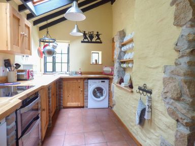 A kitchen with wooden cabinets a washing machine hanging pots and cups Old Winery Cottage Golant near Fowey