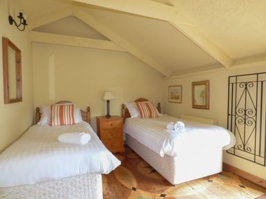 A bedroom with two single beds a wooden nightstand and wall decorations at Old Winery Cottage Golant near Fowey