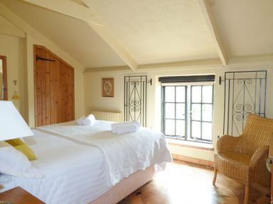 A bedroom with a bed with white linens wicker chair and a window with black trim at Old Winery Cottage Golant near Fowey