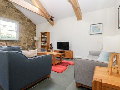 A living room with wooden beams stone wall sofas and a television at Wheal Grey in Praa Sands