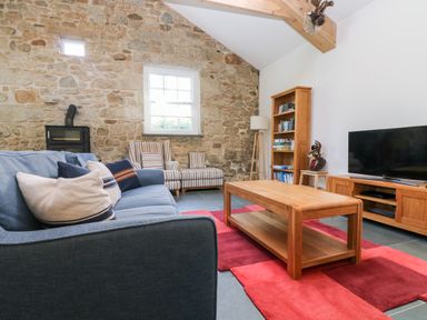 A living room with a blue sofa striped armchairs wooden coffee table bookshelf and television at Wheal Grey in Praa Sands