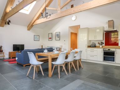 An open plan dining and living area with a wooden dining table and white chairs next to a kitchen with white cabinets and a blue sofa in Wheal Grey in Praa Sands