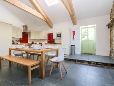 A kitchen with wooden dining table and bench white chairs green door and wooden beams at Wheal Grey in Praa Sands