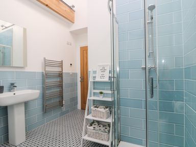 A bathroom with a shower, sink, towel rack, and shelving with baskets at Wheal Grey in Praa Sands