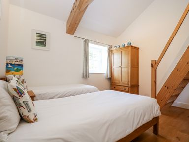 A bedroom with two single beds a wooden wardrobe and a wooden staircase at Wheal Grey in Praa Sands