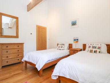 A bedroom with two single beds a wooden dresser a bedside table a lamp and a wall mirror at Wheal Grey in Praa Sands