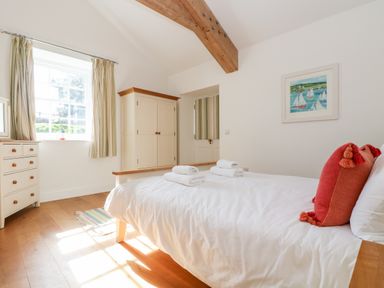 A bedroom with a bed with white linens and folded towels a wooden wardrobe a window with curtains and a framed painting on the wall at Wheal Grey in Praa Sands