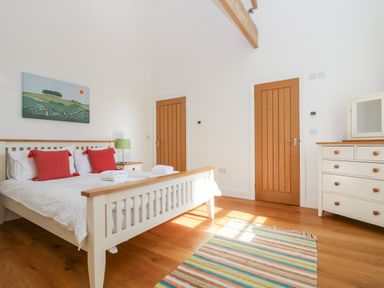 A bedroom with a bed with red pillows two wooden doors and a chest of drawers at Wheal Grey in Praa Sands