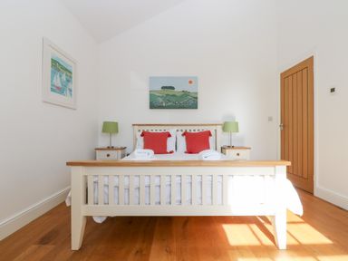 A bedroom with a wooden bed white bedding red pillows two bedside tables with green lamps and paintings on the wall at Wheal Grey in Praa Sands