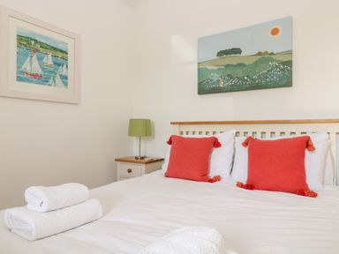 A bedroom with a bed with white linens and red pillows a bedside table with a green lamp and two paintings on the walls at Wheal Grey in Praa Sands