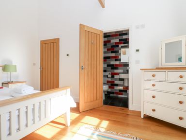 A bedroom with a bed side table and lamp a dresser with mirror and an open door leading to a bathroom at Wheal Grey in Praa Sands