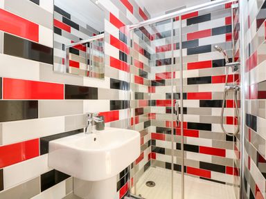 A bathroom with a sink and a glass-enclosed shower with red black gray and white tiles at Wheal Grey in Praa Sands