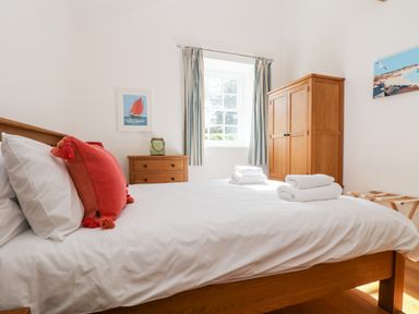 A bedroom with a wooden bed with white bedding and red cushions and wooden wardrobe at Wheal Grey in Praa Sands